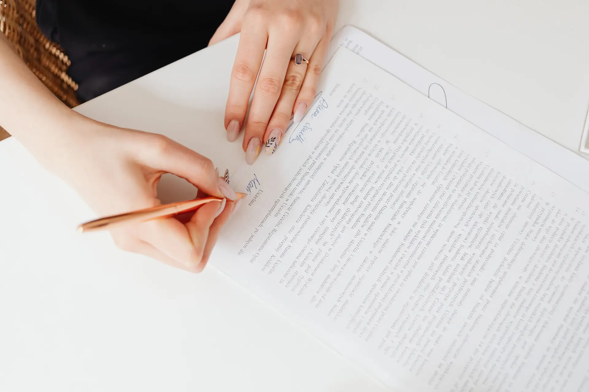 Manos firman con una pluma un documento impreso sobre una mesa de trabajo