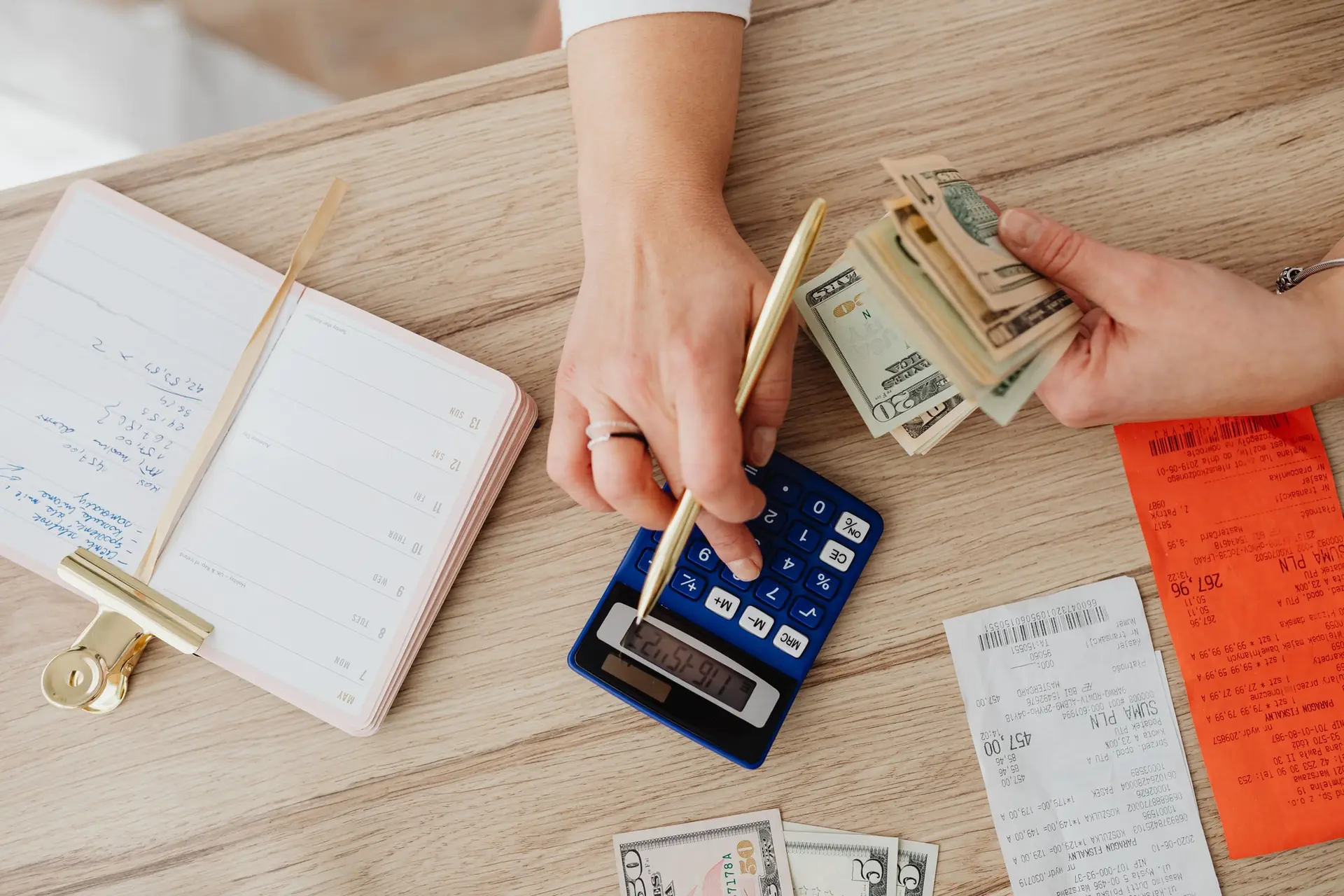 Manos contando billetes y usando una calculadora sobre un escritorio de madera con recibos y un cuaderno de cuentas